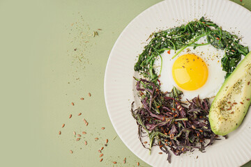 Plate with tasty fried egg, avocado and greens on green background