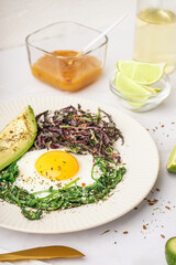 Plate with tasty fried egg, avocado and greens on light background
