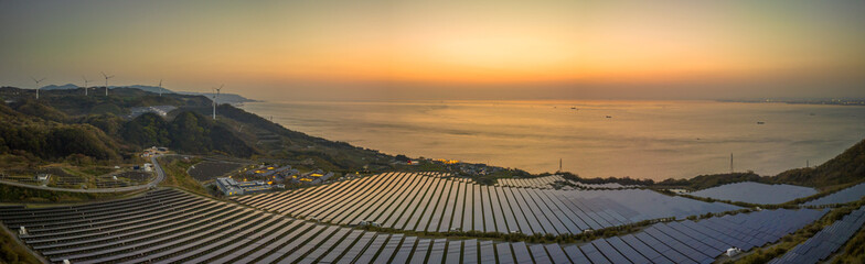 Panoramic view of solar panels and turbines on coastal energy farm at sunset - 591322760