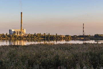 Obraz premium The old waste incinerator plant on a lake, with smoking chimneys against a colorful sky. It also causes air and environmental pollution.