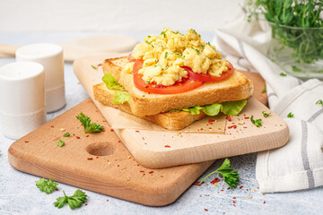 Wooden board with tasty scrambled eggs sandwich on table