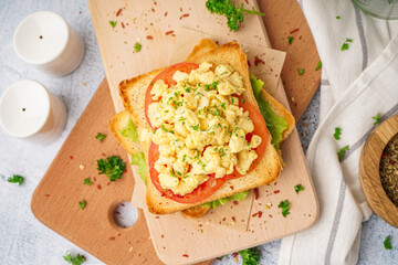 Wooden board with tasty scrambled eggs sandwich on table