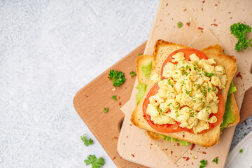 Wooden board with tasty scrambled eggs sandwich on table