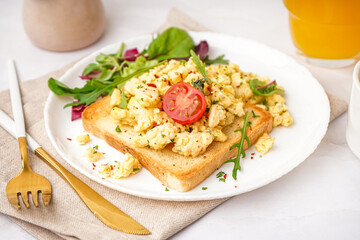 Plate with tasty scrambled eggs sandwich and salad on light background