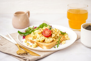 Plate with tasty scrambled eggs sandwich and salad on light background