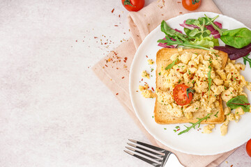 Plate with tasty scrambled eggs sandwich and salad on light background