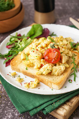 Plate with tasty scrambled eggs sandwich and salad on grey background