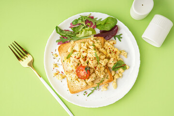 Plate with tasty scrambled eggs sandwich and salad on green background