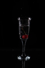 A glass of water and a cherry falling into the water