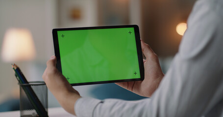 Freelance worker at home holding a tablet computer with green template screen, watching a webinar, studying online 