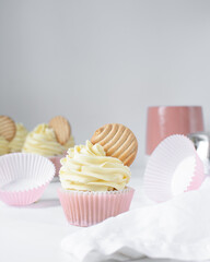 Pink cupcakes with tall american buttercream swirl and cookie garnish, cupcakes in pink liners with a tall vanilla buttercream and a cookie, birthday cupcakes on a white background