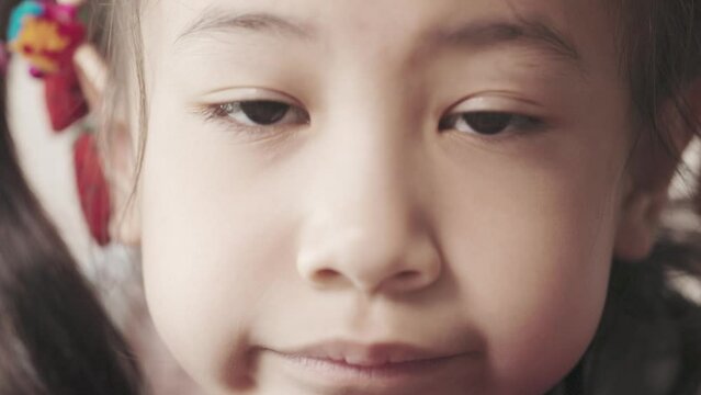 Close up 4K with slow motion of 6 years old Asian girl who is waiting with sad and boring shows beautiful face and eyes. It shows concept of unhappy and worried child for parental problem.