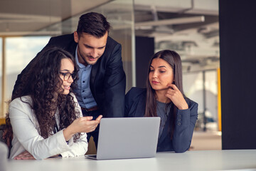 Business team collaborating on project together, using laptops. Business colleagues in casual working together in contemporary office space.