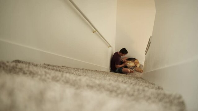 Man plays and pets large fluffy dog at bottom of stairs in home
