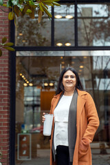 Confident mature Indian woman in casual clothes, smiling camera, standing against loft urban building