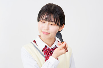 フェイスブラシを使ってメイクする女子高生　白背景