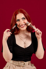 Stylish woman holding make-up brushes while posing against an isolated background.