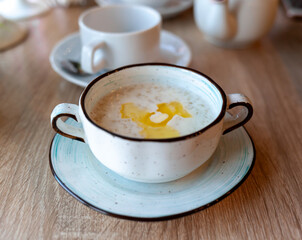 A beautiful white plate with oatmeal porridge and butter on the table. Perfect breakfast in the city cafe with oatmeal, coffee and tea on the round wooden table.