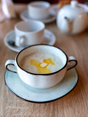 A beautiful white plate with oatmeal porridge and butter on the table. Perfect breakfast in the city cafe with oatmeal, coffee and tea on the round wooden table.