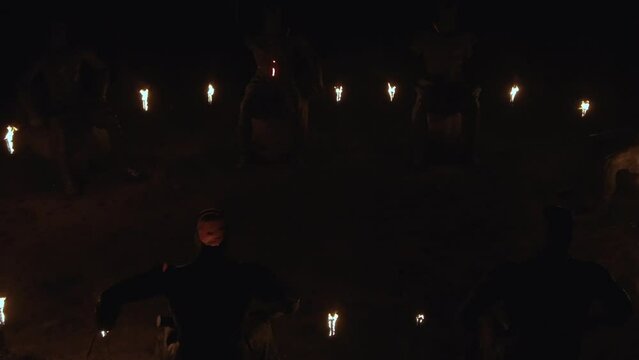 Large humanoid sit illuminated by flicker of torches at night, aerial