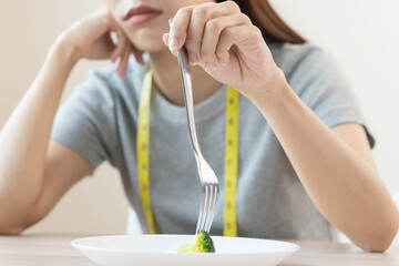 Anorexia, unhappy beautiful asian young woman, girl on dieting, hand holding fork at broccoli in...