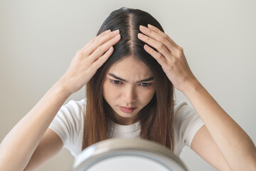 Damaged Hair symptom, face serious asian young woman, girl worry about balding, looking at scalp in mirror, hand in break into front hair loss, thin problem. Health care treatment for beauty concept. - obrazy, fototapety, plakaty