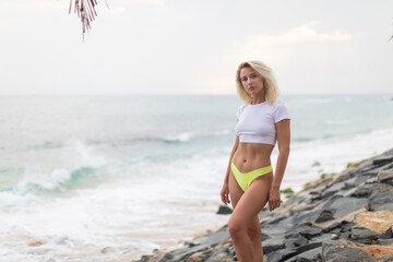 Fototapeta premium Blonde woman in a white cropped t-shirt on the ocean.