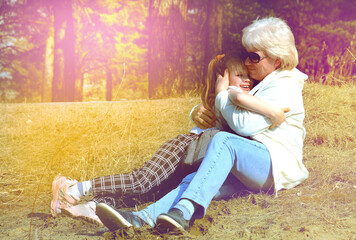 Happy grandmother with granddaughter together outdoors sitting on grass.  Happy  time. Soft sunlight and intentional soft blur foocus. Cinematic atmospheric mood