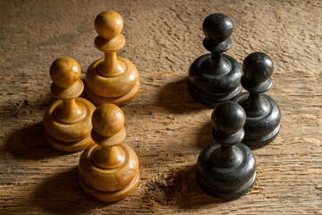 Old wooden chess. Black and white pawns stand in opposition. Chess against the background of rough wood.