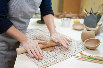 Obraz na płótnie Canvas Hobbies concept - A woman ceramist rolls clay with a rolling pin in a pottery workshop