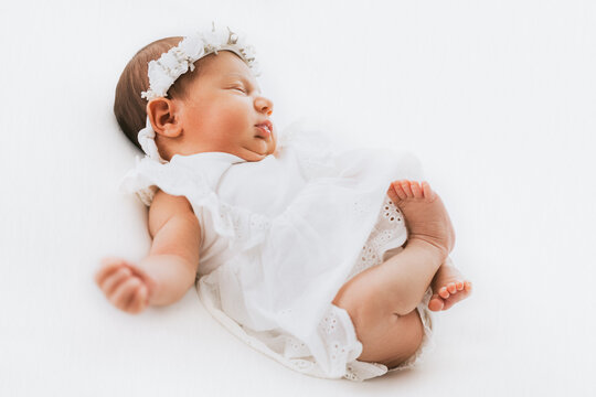 Newborn baby girl portrait, photographed in studio. Dressed in white dress.