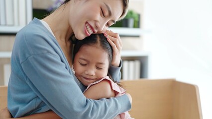 Attractive beautiful Asian mother and cute daughter sitting and hugging at cozy sofa couch living...