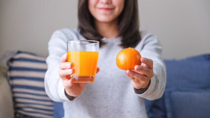 Closeup image of a young woman holding an orange and drinking fresh orange juice at home