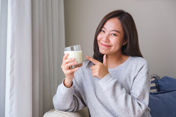 Portrait image of a young woman holding and pointing finger at a glass of fresh milk
