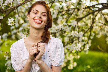 Fototapeta premium portrait of an emotional woman showing her tongue in a blooming garden