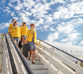 Cheerful stewardesses walking down airplane stairs under cloudy sky