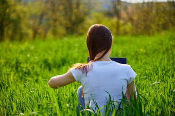 woman with laptop sitting with her back to the camera in a field