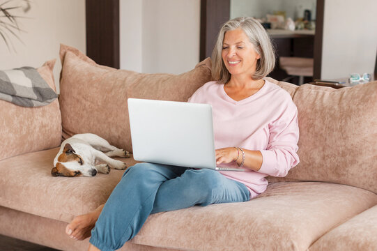 mature woman using wireless laptop apps browsing internet sit on sofa
