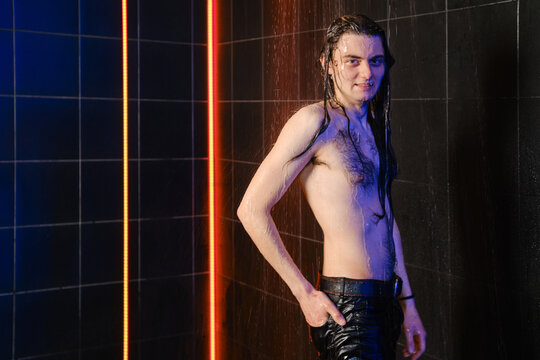 Cheerful man with long hair posing under water jets in shower