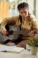 Concetrated teenage girl playing guitar at home and learning new melody