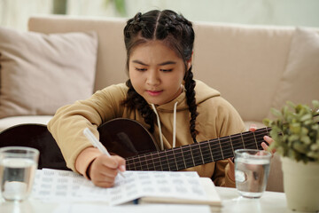 Teenage girl playing guitar and composing new song