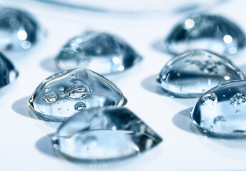 Drops of hyaluronic acid with bubbles front view, macro. Cosmetic texture on a blue background, liquid, transparent product.