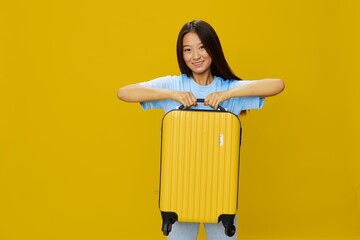 Asian woman traveling with yellow suitcase and tickets with passport in hand, tourist traveling by plane and train with luggage on yellow background in blue T-shirt and jeans