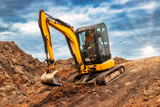 Mini excavator at the construction site on the edge of a pit against a cloudy blue sky. Compact construction equipment for earthworks. An indispensable assistant for earthworks.