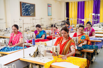Indian women group working on sewing machine at textile factory.