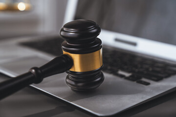 Symbolizing justice and legal authority, golden balanced scale and gavel on desk with laptop in law...