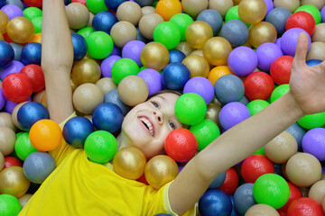Fototapeta na wymiar A happy girl is having fun playing with colorful balls in the game center