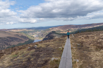 Hiker woman walking on wooden path through wicklow mountains