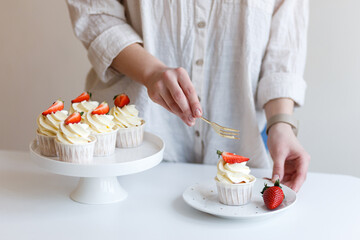 Obraz na płótnie Canvas young woman cook tastes cream cupcake with fresh strawberries