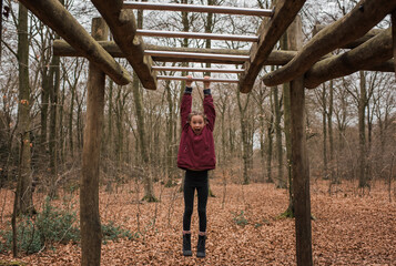 Girl hanging on monkey bars in the forest